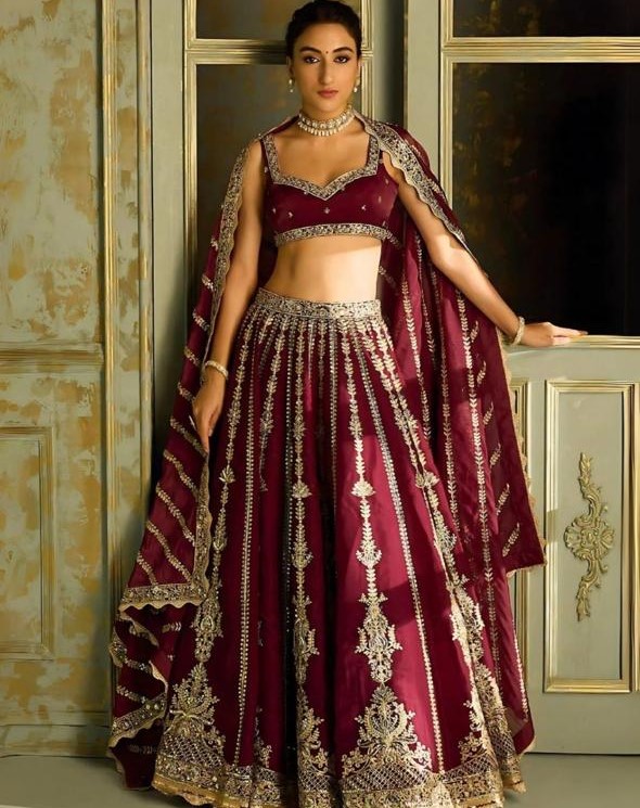 A stunning deep maroon bridal lehenga with intricate gold embroidery, perfect for brides who want a royal and elegant wedding look.