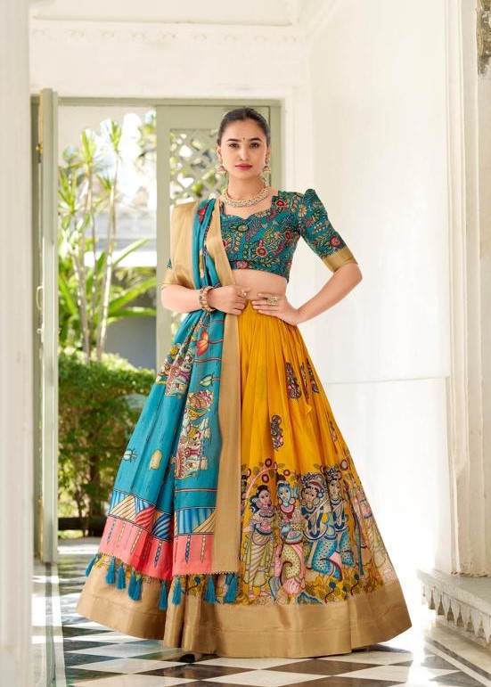 Woman wearing a vibrant hand-painted Pattachitra lehenga set, featuring a mustard yellow skirt with mythological motifs, a teal blouse with traditional artwork, and a matching teal dupatta with intricate designs, styled with gold borders and traditional jewelry.